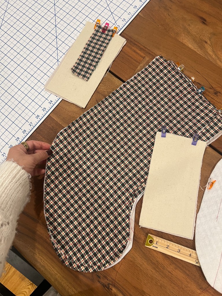 a hand holding a stocking-shape piece of fabric, which seems to be an in-progress sewing project. there are various other sewing items in this photo 