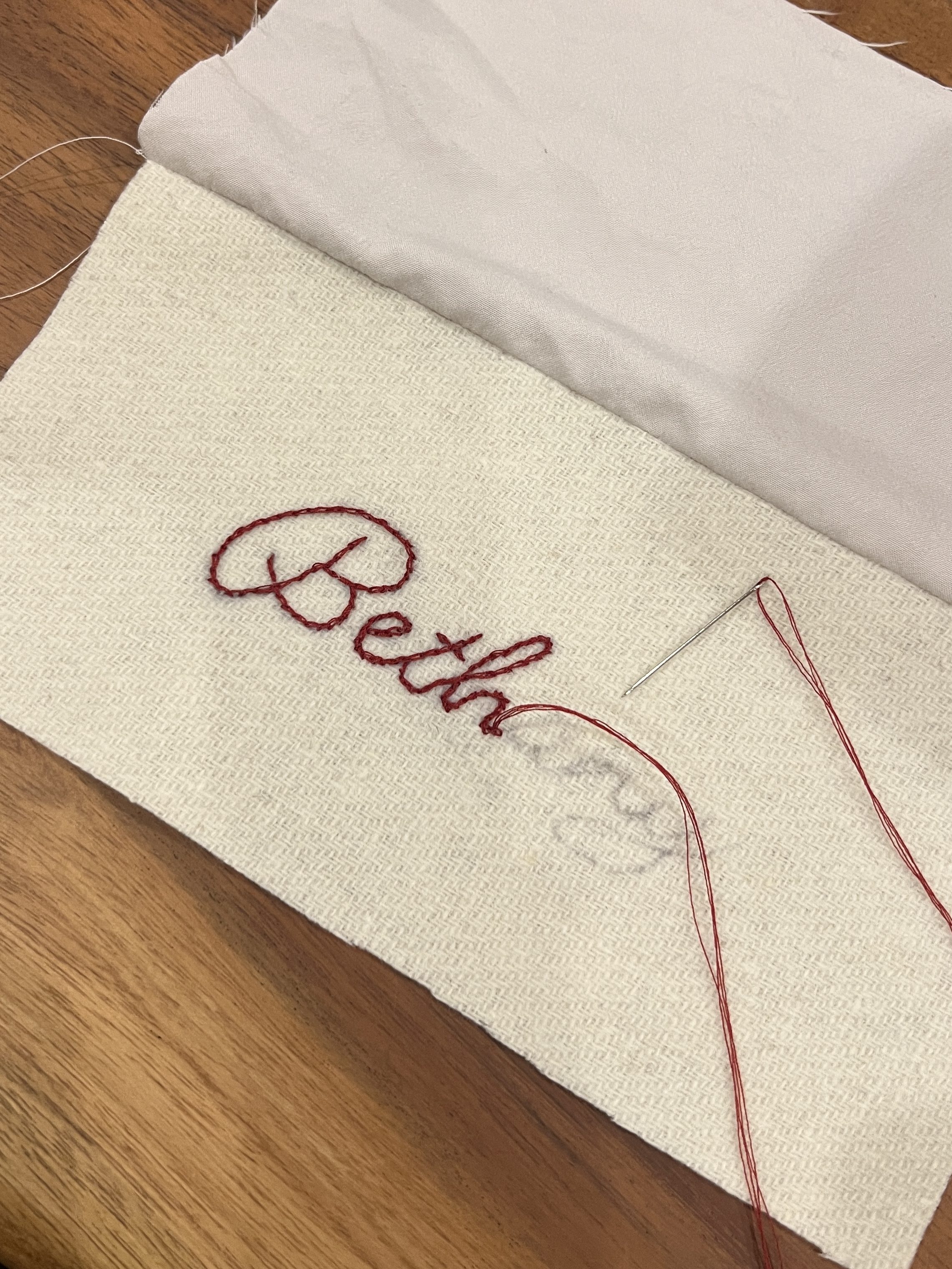 embroidery spelling out Bethany in red thread on a woven woolen cream fabric 