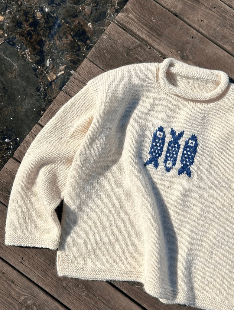 a knit white sweater with three blue knitted fish on it 